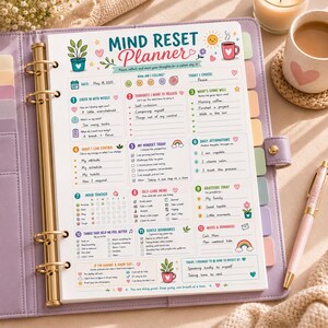 Puede incluir: Una carpeta de seis anillas de color lavanda que contiene una p&aacute;gina de Mind Reset Planner con secciones para registros diarios, seguimiento del estado de &aacute;nimo y gratitud. La p&aacute;gina presenta ilustraciones coloridas de plantas, un sol y una taza.