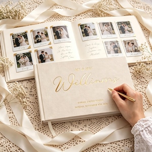 May include: A cream-coloured wedding guest book with gold foil text reading MR & MRS Williams, Hawaii, United States, Sunday, November 8th, 2026. The open book displays pages with polaroid-style photos and handwritten notes in gold corners.