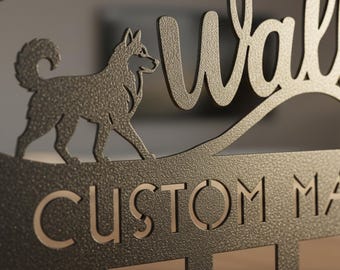 Pode incluir: Um porta-chaves de metal cinza escuro para parede, com a silhueta de um cão e as palavras "Welcome" e "Custom Made". O porta-chaves tem um acabamento texturizado e vários ganchos para chaves.