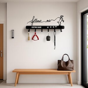 May include: Black metal dog leash holder with the words "follow me" and "CUSTOM NAME". The holder has hooks for leashes and accessories. A wooden bench and a brown leather tote bag are in the foreground.