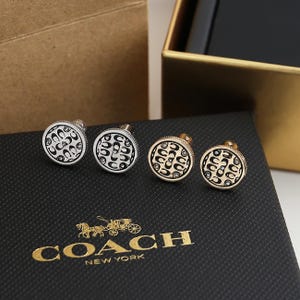 May include: Four Coach cufflinks with a circular design featuring the Coach logo in black and silver or gold. The cufflinks are displayed on a black box with the Coach logo in gold.