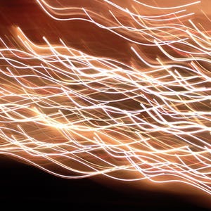 May include: Abstract image with a blurred effect, featuring numerous white and yellow wavy lines against a dark brown and black background. The lines appear to be glowing, creating a dynamic and energetic visual.