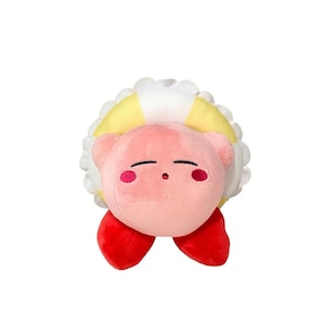 Könnte beinhalten: Ein rosa Plüschtier mit roten Füßen und rosigen Wangen. Die Figur ist von einem gelb-weißen kreisförmigen Design umgeben. Das Spielzeug hat einen neutralen Gesichtsausdruck.