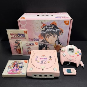 May include: A pink Sega Dreamcast game console set, including the console, controller, and a small screen. The set includes game cases and a box with anime artwork. The console and controller have Japanese text.