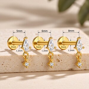 May include: Three gold-tone labret earrings with S925 stamped on the flat backings. Each features a kite-shaped clear stone and a small dangling charm with a tiny clear stone. Measurements shown are 5mm, 6mm, and 8mm lengths with 1.2mm thickness.