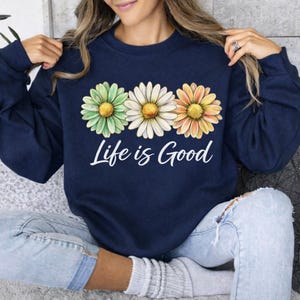 May include: A set of three ceramic mugs with a speckled, cream-colored glaze. Each mug features a different hand-painted floral design in shades of blue, green, and yellow. The mugs have a simple, rounded shape and a comfortable handle.