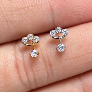 May include: Two small stud earrings, one in gold tone and one in silver tone. Each earring features a curved arch set with three clear round stones, with a single dangling round stone suspended from the center of the arch by a small metal link.