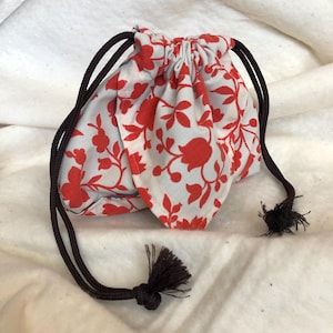 May include: A small drawstring pouch with a floral pattern in red on a white background. The pouch has a dark brown drawstring and tassel. The fabric appears to be cotton or a similar material.