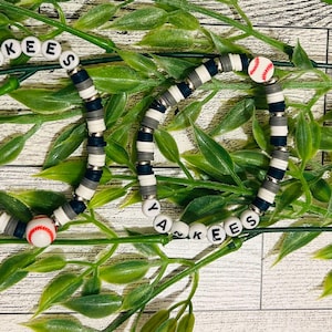 May include: Two beaded bracelets with a baseball theme. The bracelets feature white, navy blue, and grey beads, with the word "Yankees" spelled out in white letter beads. Baseball-shaped beads are also included.