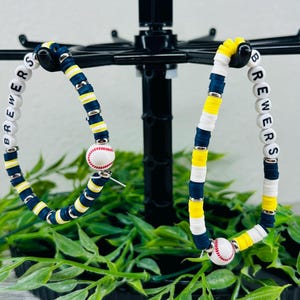May include: Two beaded bracelets featuring navy blue, yellow, and white clay discs with silver-toned spacers. Each bracelet includes white letter beads spelling BREWERS and a round bead designed to look like a miniature baseball with red stitching.