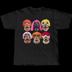 May include: Black t-shirt with a graphic of six monster masks with different hair colours, such as red, pink, and yellow. The masks have sharp teeth and are set against a black background. The design is centered on the shirt.