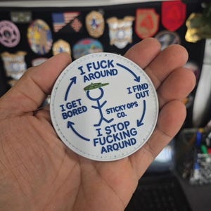 May include: A white, circular patch with blue stitching and text. The patch features a stick figure and the phrases "I FUCK AROUND," "I FIND OUT," "I STOP FUCKING AROUND," and "I GET BORED." The text is in a bold, sans-serif font. The patch is from Sticky Ops Co.