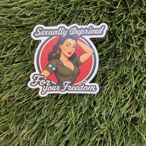 May include: A sticker featuring a vintage pin-up girl in a military-style uniform, set against a red circle. The text "Sexually Deprived" arches above the image, with "For your Freedom" below.