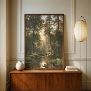 May include: A framed vertical wall art print depicting a forest landscape with a calm stream, tall trees, and soft golden sunlight filtering through the canopy. The artwork is displayed on a wooden sideboard next to a white vase and a floor lamp.