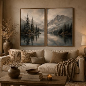 May include: Two framed landscape wall art prints depicting a misty mountain lake scene with evergreen trees and rocky shores. The artwork features muted earth tones, soft lighting, and reflections on the water surface, displayed side by side.