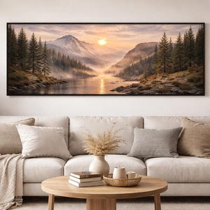 Könnte beinhalten: Ein gerahmter Landschaftskunst-Druck zeigt eine Berglandschaft mit einem Fluss, Bäumen und einem Sonnenuntergang. Das Kunstwerk wird über einem beigen Sofa mit Kissen und einem Holztisch ausgestellt. Die Farbpalette ist warm und natürlich.