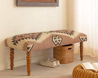 Op de afbeelding: Decoratieve bank met een bruin en beige patroon en houten poten. De bank heeft een geweven ontwerp en staat tegen een muur. Een geweven mand en een paar schoenen staan naast de bank.