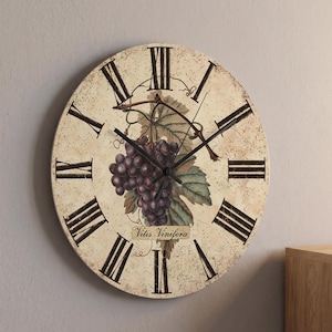 May include: A round wall clock with a distressed cream-colored face featuring black Roman numerals and a central illustration of purple grapes and green leaves. The text Vitis Vinifera is printed below the grapes with black clock hands.