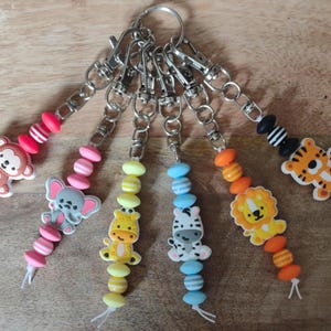 May include: A collection of keychains with animal-themed charms. Each keychain features a different animal: a monkey, elephant, giraffe, zebra, lion, and tiger. The charms are attached to beaded strands in various colors.