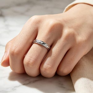 May include: A silver-toned metal ring featuring a repeating geometric diamond-shaped pattern engraved around the entire outer band. The ring has a polished finish with beveled edges, creating a textured look that catches the light across the surface.