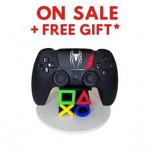 May include: Black game controller with a white spider logo and red accents. The controller sits on a white stand with colorful game symbols. The text "ON SALE + FREE GIFT*" is in red at the top.