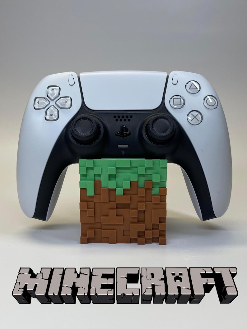 Peut inclure: Une manette PlayStation 5 blanche et noire repose sur un bloc pixelis&eacute; marron et vert, rappelant un paysage Minecraft. Le mot "Minecraft" est affich&eacute; en police pixelis&eacute;e 3D en dessous.
