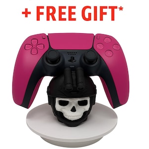 May include: A magenta and black video game controller rests above a black skull-shaped stand with a white skull face. The text "ON SALE + FREE GIFT*" is displayed in red above the controller.