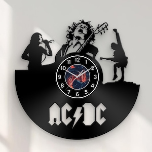 Könnte beinhalten: Schwarze Vinyl-Schallplattenuhr mit Silhouetten einer Band, die auftritt. Das Zifferblatt hat ein farbenfrohes Design. Der Bandname AC/DC ist in weißen Blockbuchstaben darunter abgebildet.