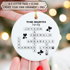 Può includere: Ornamento rotondo in ceramica bianca con cordino dorato. Il testo "THE SMITH Family" è visualizzato, con nomi scritti con tessere di lettere e icone di cuore e impronte di zampe. Lo striscione in alto recita "A-Z LETTER TILES + ICONS CREATE YOUR OWN ORNAMENT • PNG".