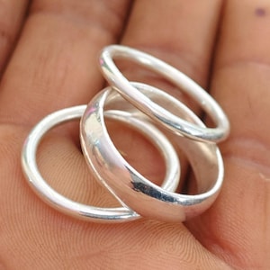 May include: Three silver rings are shown, highlighting their polished, reflective surfaces. The rings are arranged together, demonstrating their simple, elegant design. The rings are likely made of sterling silver or a similar metal.