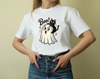 May include: White t-shirt featuring a cartoon ghost with a black cat on top. The word "Boo!" is written above the ghost. The design has a Halloween theme.