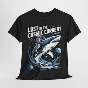 Könnte beinhalten: Schwarzes T-Shirt mit einer Grafik eines Astronauten, der auf einem blauen Hai durch den Weltraum reitet. Der Text "LOST IN THE COSMIC CURRENT" befindet sich über dem Astronauten und dem Hai. Planeten und Sterne sind im Hintergrund.