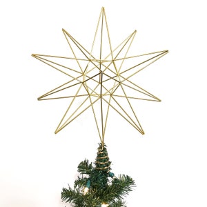 May include: Gold wire star tree topper. The star is a geometric design with multiple points. It is sitting on top of a green Christmas tree.