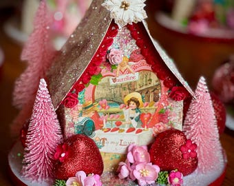 May include: A Valentine's Day themed decorative house with a glittered roof and base. The house features a vintage Valentine's Day card image, red heart accents, pink bottle brush trees, and the text "To my Love".