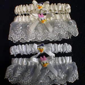 May include: Set of four white satin and lace garters with a white satin bow and a cartoon duck charm. The charms have different colored bows.