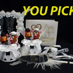 Puede incluir: Un conjunto de adorno para tarta de boda con figuras de Mr. y Mrs. Potato Head, un cuchillo para tarta en forma de corazón, un libro de visitas blanco con el texto "Wedding Guests" y dos copas de champán.