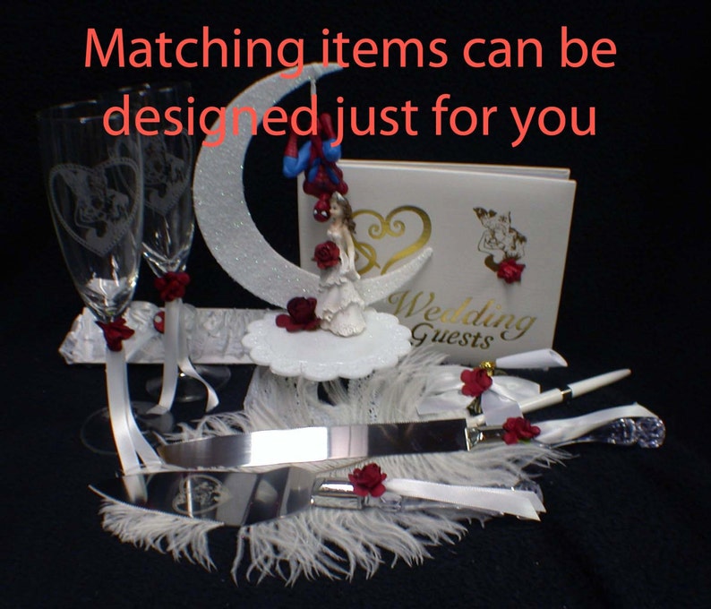 May include: Wedding cake topper with a bride and groom figurine, a white cake knife, two champagne flutes, a guest book, and a white feather boa. The cake topper features a bride and groom figurine standing on a crescent moon. The bride is wearing a white dress and the groom is wearing a blue suit. The cake knife is silver and has a white handle. The champagne flutes are clear glass and have a white ribbon tied around the stem. The guest book is white and has the words "Wedding Guests" printed on the front. The white feather boa is draped over the cake knife and champagne flutes.