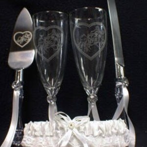 Puede incluir: Un juego de servir pastel de boda con dos copas de champ&aacute;n, un cuchillo para pastel y una liga blanca. Las copas y el cuchillo est&aacute;n grabados con un dise&ntilde;o de coraz&oacute;n.