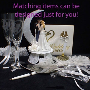 May include: Wedding cake topper set with a bride and groom figurine, a cake knife and server, two champagne flutes, a white feather boa, and a white lace garter. The cake topper features a crescent moon and the words "Wedding Guests".
