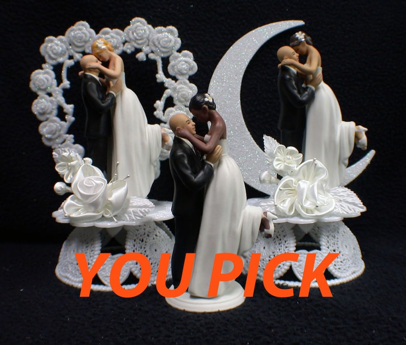 May include: Two wedding cake toppers, one with a white bride and groom in a heart-shaped frame, and the other with a black bride and groom in a crescent moon frame. Both couples are holding each other and smiling. The text "YOU PICK" is visible in the bottom center of the image.