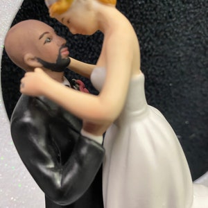 Pu&ograve; includere: Un topper per torta nuziale con una sposa e uno sposo. La sposa indossa un abito bianco e lo sposo indossa un abito nero. La sposa tiene il viso dello sposo e si guardano.