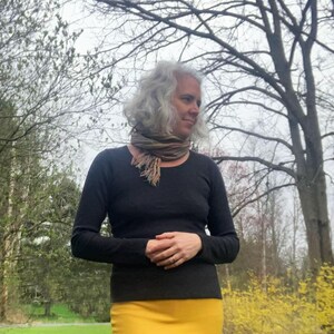 May include: A long-sleeved black shirt with a scoop neckline paired with a mustard yellow skirt and a multi-colored striped scarf featuring frayed edges. The ensemble consists of a solid dark top and a vibrant, plain yellow bottom garment.
