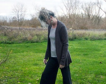 May include: A dark brown open-front cardigan worn over a light gray t-shirt, paired with wide-leg black trousers and gray ankle boots. The outfit features a layered look with long sleeves on the cardigan and a relaxed fit for the trousers.