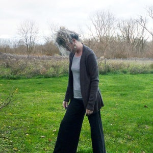 May include: A dark brown open-front cardigan worn over a light gray t-shirt, paired with wide-leg black trousers and gray ankle boots. The outfit features a layered look with long sleeves on the cardigan and a relaxed fit for the trousers.