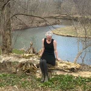 May include: A black sleeveless tank dress worn with dark gray leggings and olive green ankle boots. The dress features a scoop neckline and a simple, fitted bodice that flares slightly at the hem, providing a clean and functional silhouette.