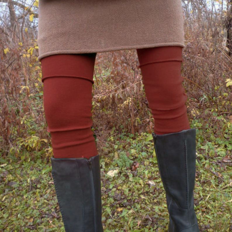 K&ouml;nnte beinhalten: Eine rostfarbene Leggings mit horizontalen N&auml;hten &uuml;ber den Knien, getragen unter einem beigen Rock und kombiniert mit schwarzen wadenhohen Stiefeln. Die Leggings ist eng anliegend und reicht vom Saum des Rocks bis zum oberen Rand der Stiefel.