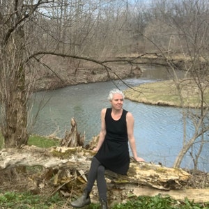 May include: A black sleeveless tank dress worn with dark gray leggings and olive green ankle boots. The dress features a simple scoop neckline and a relaxed, straight-cut silhouette that falls above the knees, providing a clean and functional look.