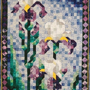 Peut inclure: Une courtepointe avec un motif de patchwork de carrés blancs, violets, verts et bleus. La courtepointe représente trois iris blancs avec des centres jaunes et des tiges vertes. La courtepointe est encadrée d'une bordure de carrés violets, verts et jaunes. Le texte "Jane L Kakey.etsy.com" est visible dans le coin inférieur droit.