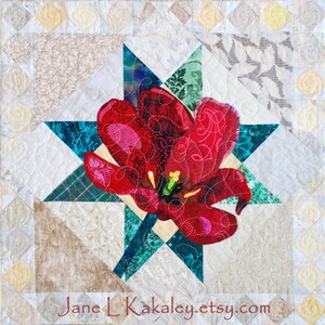 May include: A red flower with a white center is the focal point of this quilt block. The flower is surrounded by a teal and green star shape. The background is a light beige with a diamond pattern.
