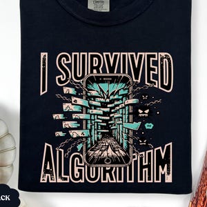 May include: Black t-shirt with the text "I SURVIVED ALGORITHM" in white and pink. The design features a smartphone with a digital maze and monster graphics. The shirt is a Comfort Colors brand.